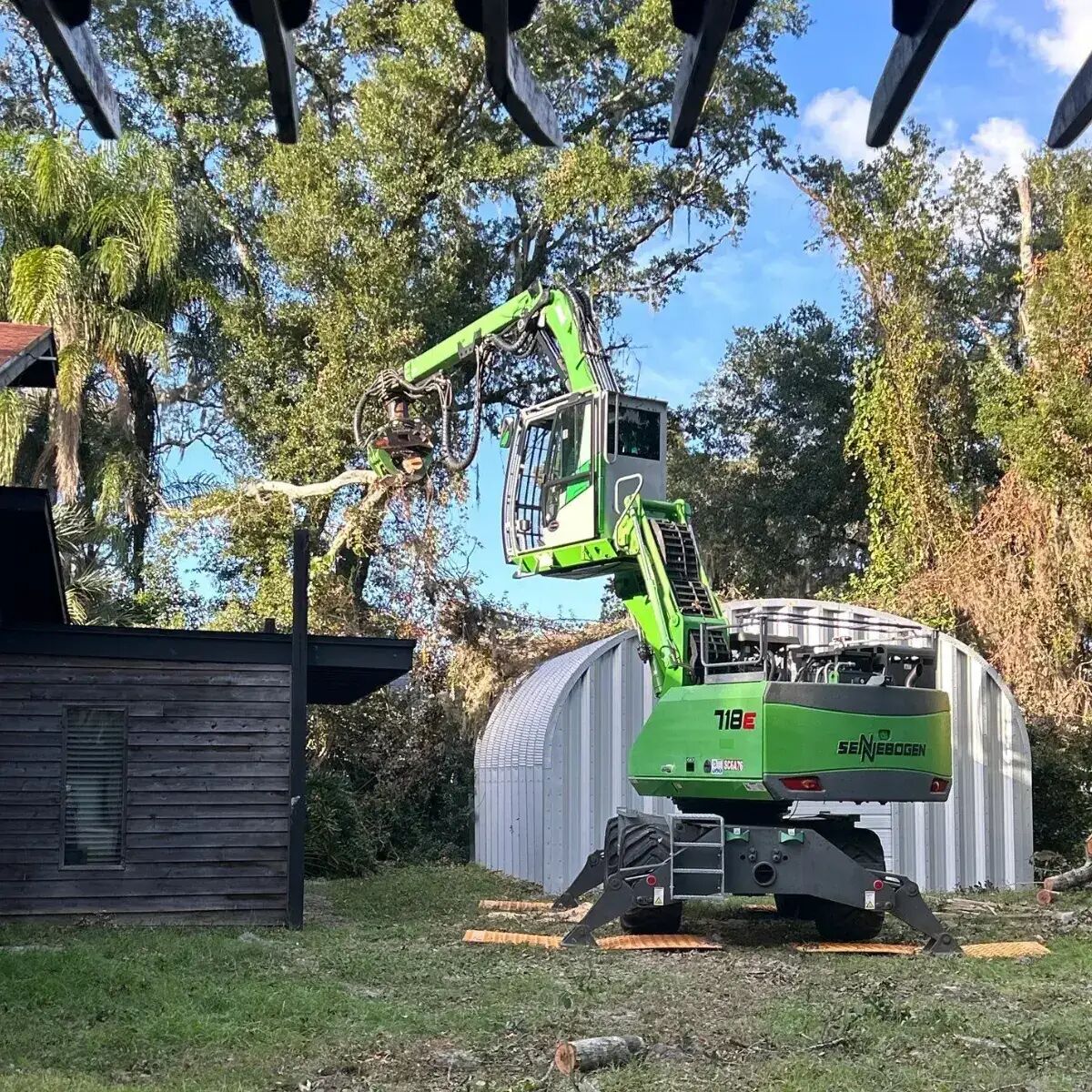Sennebogen tree handler removing a tree next to a shed