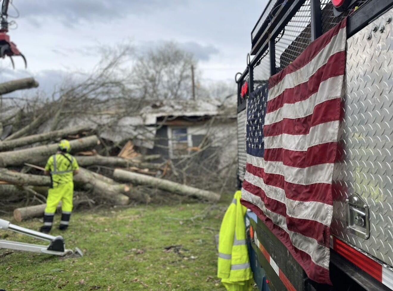 Crew member clearing tornado debris beside a Garrison McKinney truck with an American flag